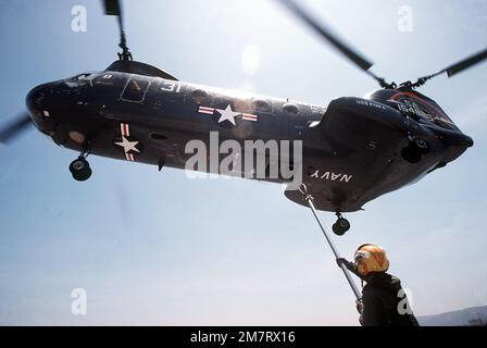 Eine linke Unteransicht eines CH-46D Sea Knight Helikopters vom Helicopter Combat Support Squadron 3 (HC-3), Ablösung 103, während er sich in Position bewegt, um einen Frachthaken aufzunehmen. Der Hubschrauber ist dem Munitionsschiff der Kilauea-Klasse USS KISKA (AE-35) zugewiesen. Land: Unbekannt Stockfoto