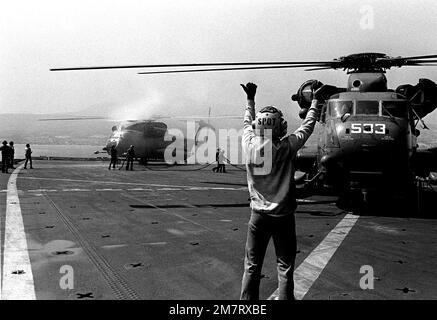 Ein Besatzungsmitglied im Cockpit leitet den Piloten eines Helicopter Mine Gegenmaßnahmen Squadron 14 (HM-14) RH-53D Sea Hallion Helikopter kurz vor dem Start vom Deck der Amphibien-Transportanlage USS NASHVILLE (LPD-13). Die NASHVILLE und die Helikopter an Bord nehmen an Übungen der Arbeitsgruppe für Minenabwehrmaßnahmen 1-81 (MCMTG 1-81) Teil, um die Fähigkeiten der sieben teilnehmenden NATO-Länder zur Minenabwehr zu erhöhen. Land: Mittelmeer (MED) Stockfoto