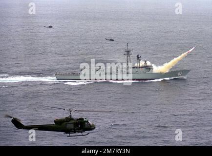 Luftaufnahme von Steuerbord der Australian Frigate HMAS CANBERRA (F-02), die ihre erste Harpoon-Rakete in der Nähe des Pacific Missile Test Center, Point Mugu, Kalifornien, startet. Drei UH-1 Iroquois Helikopter bieten Luftüberwachung des Starts. Land: Pazifik (POC) Stockfoto