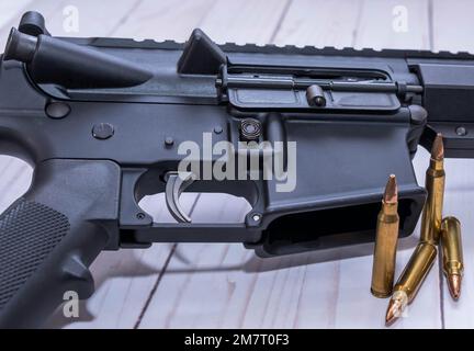 Ein AR15-Gewehr in Kaliber 223 mit vier Kugeln daneben auf weißem Holzhintergrund. Stockfoto