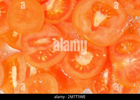 Tomaten-Nahaufnahme in Flüssigkeit mit Blasen. Scheiben roter reifer Tomaten im Wasser. Nahaufnahme frischer Scheiben roter Tomaten auf weißem Hintergrund Stockfoto