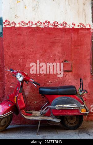 Kairo, Ägypten. November 26. 2022 süßer roter Motorroller parkt vor einer rot bemalten Wand im islamischen Viertel von Kairo in der Nähe des Khan el Khalili Ba Stockfoto