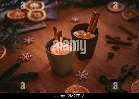 Glühwein in alten Tassen mit Zimtstroh steht auf einem alten Tisch, umgeben von Fichtenzweigen Stockfoto