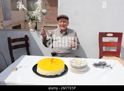 Ein älterer Mann feiert seinen Geburtstag im Familienhaus. Die Kerze ausblasen und einen Ballon halten. Stockfoto