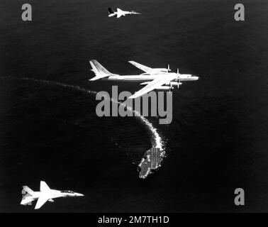 Eine Air-to-Air-Ansicht von rechts eines russischen TU-95 Tupolev Bomberflugzeugs, Center, und zwei US-Flugzeuge Navy F-14 Tomcat-Flugzeug, das als Verfolgungsflugzeuge über dem Flugzeugträger USS KITTY HAWK (CV-63) fungiert, während das Schiff nach rechts abbiegt. Die NATO-Bezeichnung des Tupolev-Flugzeugs ist Bear. Land: Unbekannt Stockfoto
