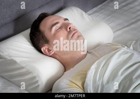 Süßer junger Mann, der auf einem orthopädischen Kissen im Bett schläft Stockfoto