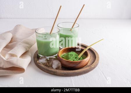 Köstlicher, gesunder Matcha Latte Tee in zwei Gläsern mit Stroh und Eisstücken auf einem runden Holztablett. Eine Alternative zum Kaffee. Belebendes Getränk Stockfoto