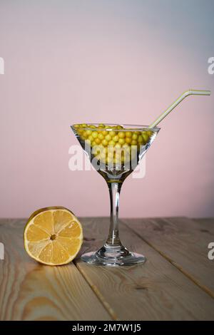 Ein Glas martini mit Vitamin C in Form eines Dragee. Mit einem Strohhalm. Daneben eine Zitronenscheibe. Das Glas steht auf Pinienbrettern. Stockfoto