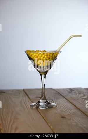 Ein Glas martini mit Vitamin C in Form eines Dragee. Mit einem Strohhalm. Das Glas steht auf Pinienbrettern. Stockfoto