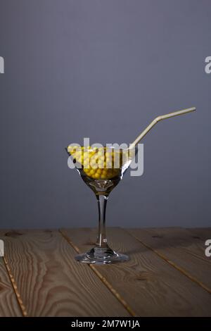Ein Glas martini mit Vitamin C in Form eines Dragee. Mit einem Strohhalm. Das Glas steht auf Pinienbrettern. Stockfoto