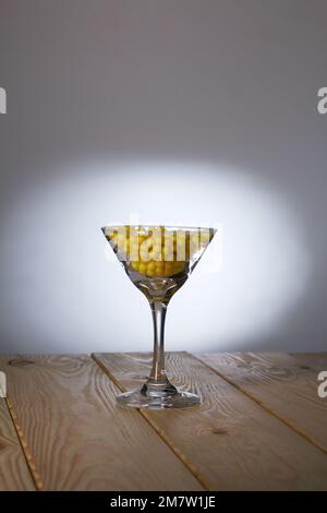 Ein Glas martini mit Vitamin C in Form eines Dragee. Mit einem Strohhalm. Das Glas steht auf Pinienbrettern. Stockfoto