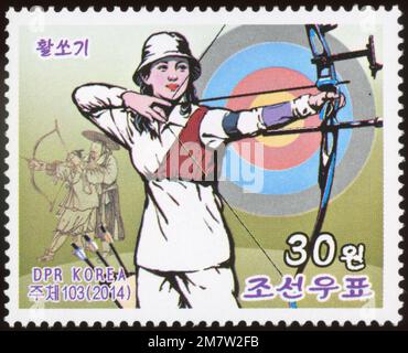 2014 nordkoreanische Briefmarke mit einer Frau, die Bogenschießen praktiziert, aus der Serie Korean Folk Customs. Stockfoto