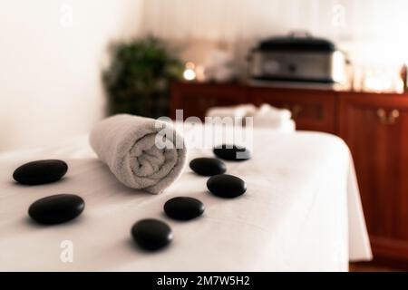 Handtuch und Lavasteine auf dem Massagetisch im Wellnesssalon. Stockfoto