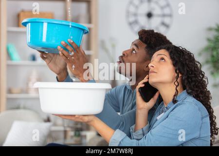 Ein junges Paar sammelt Wasser, das aus der Decke tropft Stockfoto