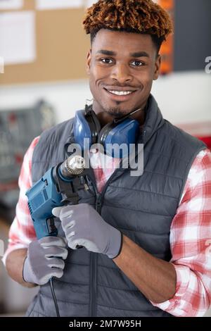 Lächelnder Handwerker mit Elektrobohrer in den Händen, der in der Werkstatt steht Stockfoto