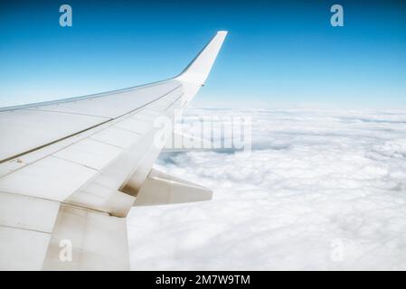 Blick aus dem Fenster des Flugzeugs auf den Himmel und die Wolken darunter. Klappen am Flügel des Flugzeugs Stockfoto