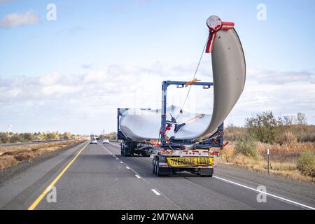 Leistungsstarker industrieller Sattelschlepper mit zusätzlichem Transportwagen transportiert Überladungen mit einem superlangen Schild einer Windturbine und einer Begleitperson ca. Stockfoto