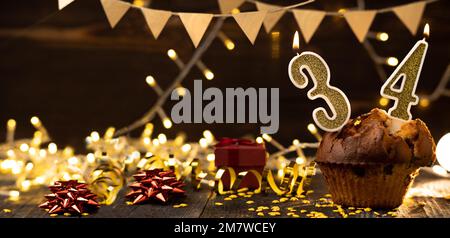 Geburtstagskerze Nummer 34 in Cupcake vor Lichtern und Holzhintergrund. Speicherplatz kopieren. Banner Stockfoto