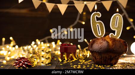 Nummer 69 goldene festliche brennende Kerzen in einem Kuchen, hölzerner Feiertagshintergrund. 69 Jahre seit der Geburt. Das Konzept der Geburtstagsfeier Stockfoto