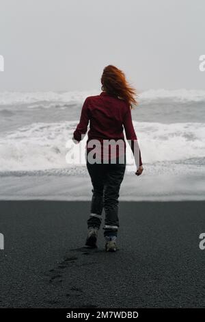 Frau, die am Strand Reynisfjara spaziert und malerische Fotos macht Stockfoto