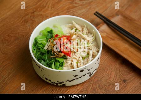 Indonesischer Reisbrei mit zerkleinertem Hühnerfleisch, serviert mit Gemüse und Gewürzen Stockfoto