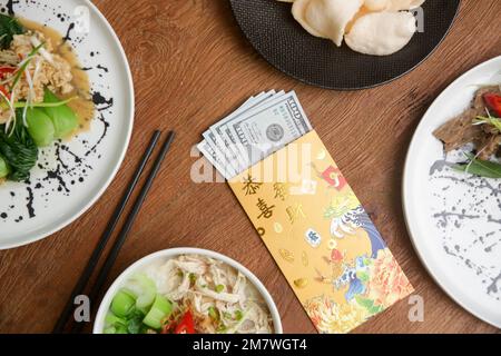 Essen am Mond-Silvester auf dem Tisch mit goldenem Umschlag gefüllt mit Geld als Zeichen des Glücks im neuen Jahr. Stockfoto