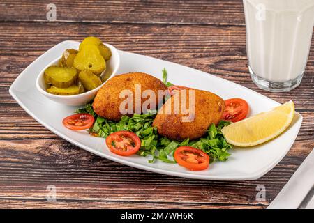 Kibbr oder Ili Kofte auf einem weißen Porzellanteller mit Gurken und Salat Stockfoto