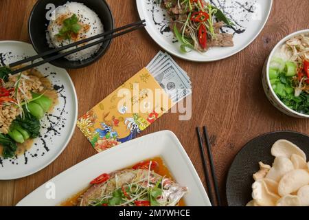 Essen am Mond-Silvester auf dem Tisch mit goldenem Umschlag gefüllt mit Geld als Zeichen des Glücks im neuen Jahr. Stockfoto