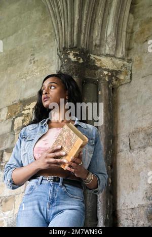 Eine junge Frau mit einem Buch, das an einer mittelalterlichen Säule im Kloster steht. Stockfoto