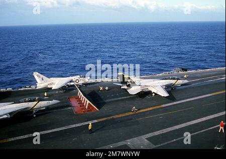 Ein F-14 Tomcat-Flugzeug wartet hinter den Deflektorplatten, während eine weitere F-14 von Fighter Squadron 84 (VF-84) sich auf den Start während des Flugbetriebs an Bord des nukleargetriebenen Flugzeugträgers USS CARL VINSON (CVN-70) vorbereitet. Ein 7E Corsair II-Flugzeug vom Light Attack Squadron 82 (VA-82) ist startbereit für den Start auf dem Hafenkatapult. Land: Unbekannt Stockfoto