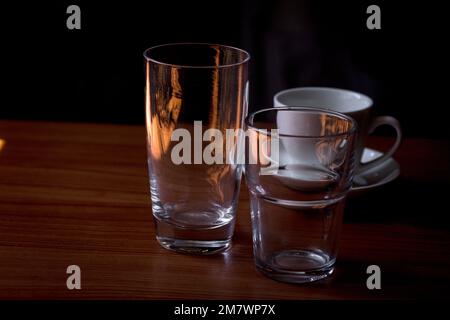 Wassergläser aus transparentem Glas und Kaffeetassen auf einem Holztisch. Stockfoto