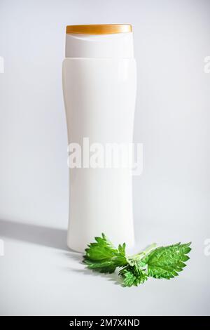 Eine Flasche Shampoo. Balsam mit Nesselextrakt in einer weißen Flasche auf weißem Hintergrund mit Studiolicht und Schatten. Heilkraut für die Pflege Stockfoto