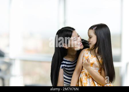 Porträt einer glücklichen asiatischen Mutter mit ihrer kleinen Tochter. Verschwommener heller Hintergrund. Stockfoto