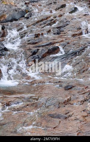 Wunderschöne Textur aus schwarzschokoladenbraunem Granit, gewaschen durch fließendes Wasser des alpinen Baches, Nahaufnahme, vertikaler Schuss, Aosta-Tal, Italien Stockfoto