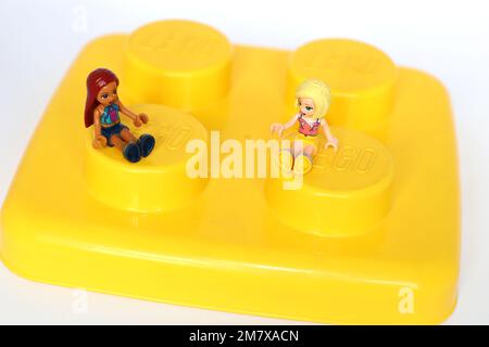 2 kleine lego-Mädchen, die auf einem riesigen gelben lego-Block sitzen. Editorial use Stockfoto