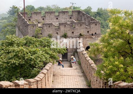 Peking, China - 17. August 2010: Tausende Touristen besuchen täglich die Chinesische Mauer. Zwei Frauen, die sich vom langen Weg erholen. Ein Blick auf sein Handy Stockfoto