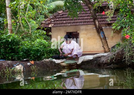 Allepy, Indien - 7. September 2012. Eine Indianerin wäscht Geschirr und Besteck am Rand eines der Kanäle von Alappuzha Stockfoto