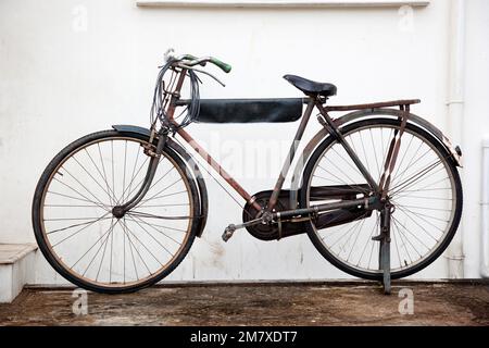 Ein altes rostiges Fahrrad, das vor einer weißen Wand geparkt ist Stockfoto