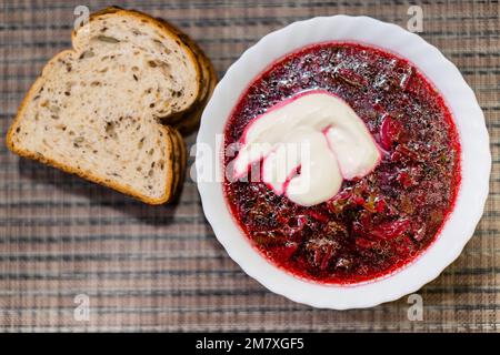 Borschtsch - saure Suppe, die in Osteuropa üblich ist - mit roten Roten Bete und saurer Sahne - ein Stück Brot Stockfoto