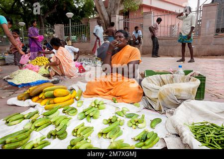 Madurai, Indien - 11. September 2012. Auf dem Abendmarkt in der Stadt Madurai in Indien, in der Monsunzeit, isst der Verkäufer einige Fuits, während er auf einen wartet