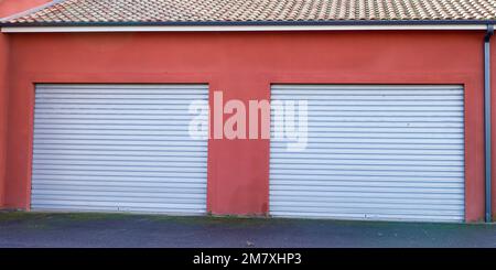 Die rote Fassade des Industriegebäudes schloss zwei graue Rollladentore Stockfoto