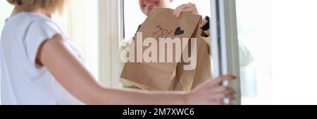 Frau erhält Paket vom Kurier mit Herz vor der Haustür Stockfoto