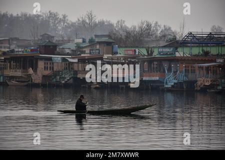 Srinagar, Indien. 11. Januar 2023. Ein Mann rudert mit seinem Boot über den Dal-See, während es in Srinagar regnet. Das MET-Büro hat für viele Orte in Kaschmir einen leichten Schneefall vorhergesagt. Die Ebenen im Tal werden voraussichtlich mit leichtem bis moderatem Schnee bedeckt sein. Leichter Schneefall, mit Regenfällen in den Ebenen von Jammu, ist wahrscheinlich an vielen Orten, sagte sie. Kredit: SOPA Images Limited/Alamy Live News Stockfoto