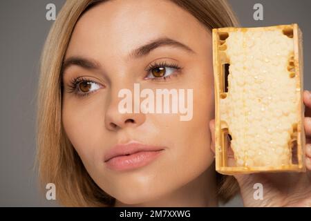 Nahaufnahme einer jungen Frau mit süßem Honig in Wabe isoliert auf grauem Stockbild Stockfoto
