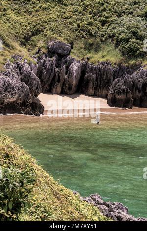 Ein Mann badet in einem kleinen, leeren Strand, umgeben von Felsen und großen Steinen mit Vegetation in der Stadt Kantabrien, Spanien, Europa Stockfoto
