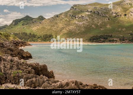 Drei Frauen baden am Strand von Oriñon mit Felsen und dem grünen Berg im Hintergrund in Kantabrien, Spanien Stockfoto