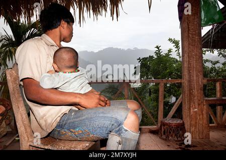 Luang Nam Tha, Laos, 19. Juli 2009. In einem Dorf des ethnischen Khamu im Norden von Laos hält ein junger Mann nach einem harten Arbeitstag seinen Sohn beim Watc zum Schlafen Stockfoto