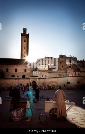 Fez, Marokko-25. April 2014: Sonnenuntergang auf einem Platz, wo Marokkaner Lebensmittel und Kleidung auf einem kleinen Markt verkaufen, viele Leute beobachten und kaufen, andere Restaurants Stockfoto