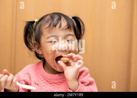 Ein glückliches Kleinkind, das Schokoladeneis in einer Schüssel mit unordentlichem Gesicht isst Stockfoto