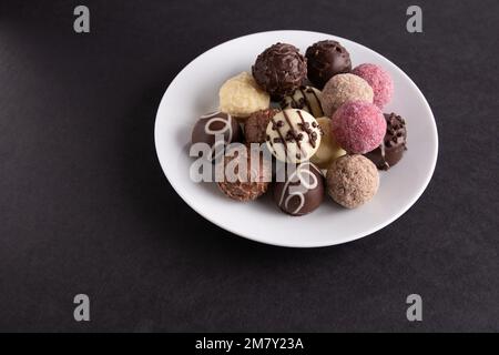 Fotomix verschiedener Schokolade auf einer weißen Platte auf schwarzem Hintergrund Stockfoto